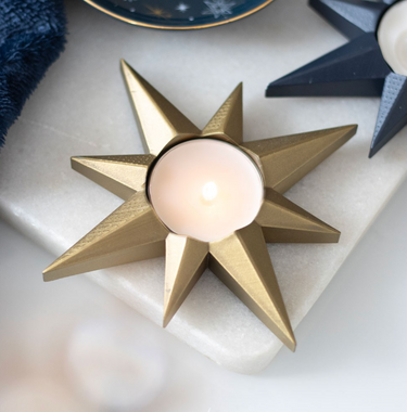 Gold star-shaped candle holder with a lit candle on a white surface.