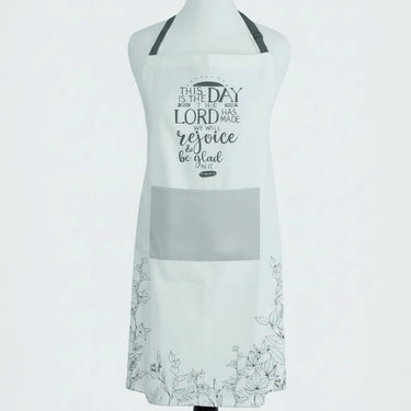 A white bib apron displayed on a mannequin torso against a light gray background. The apron features a dark gray chest pocket, black neck strap, and black printed text on the front reading 'THE DAY IS THE DAY THE LORD HAS MADE we rejoice and be glad'.