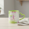 A white ceramic mug with a bright green handle and interior, decorated with pink watercolor flowers and the text 'Serve ONE Another in love Galatians 5:13' alongside pink hearts, on a white background.