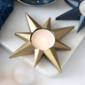 Gold star-shaped candle holder with a lit candle on a white surface.