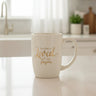 An off-white ceramic coffee mug with a gold foil inscription that reads 'For God so Loved.